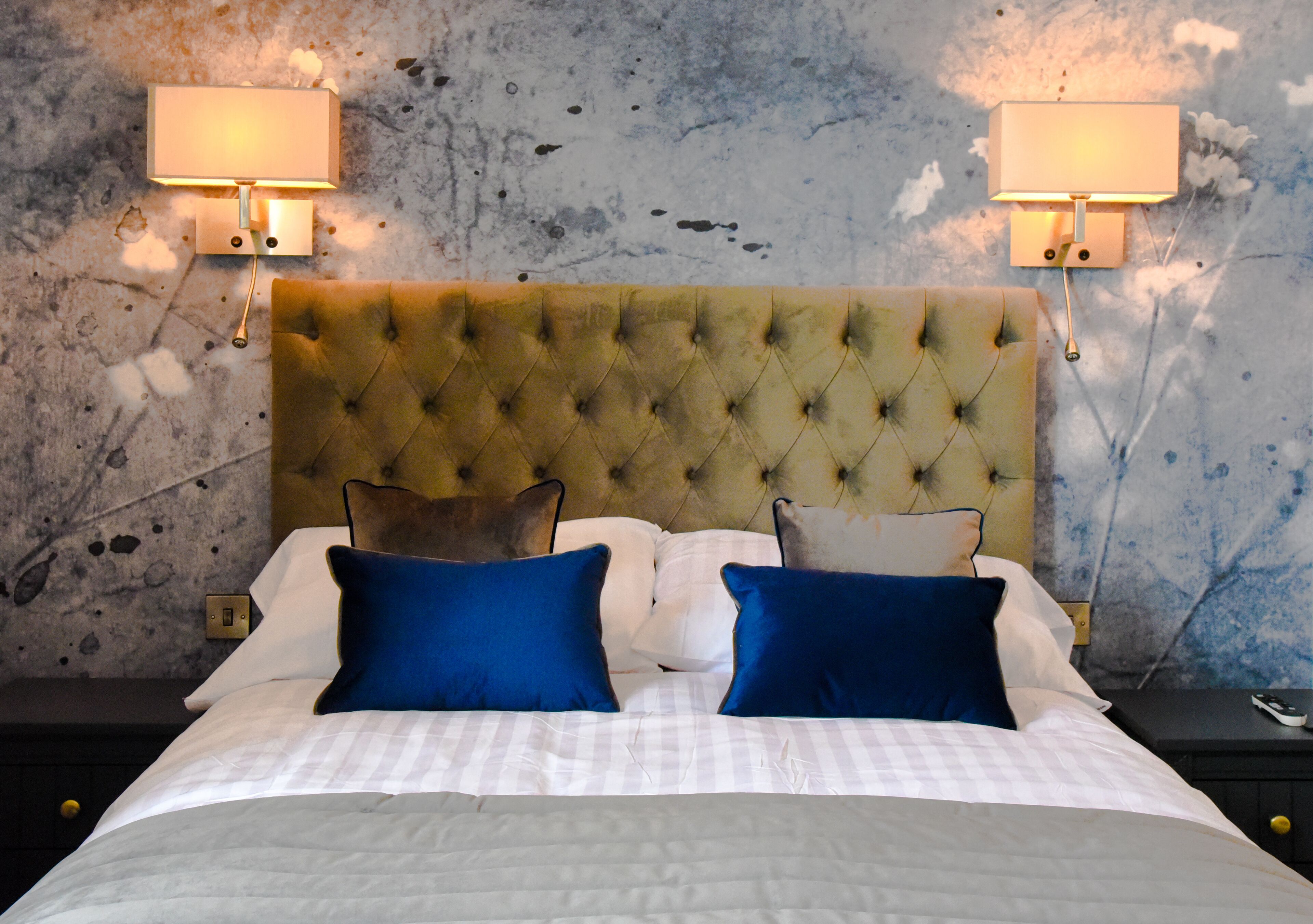 A neatly made bed with a tufted headboard, two bedside lamps, and a textured wall.