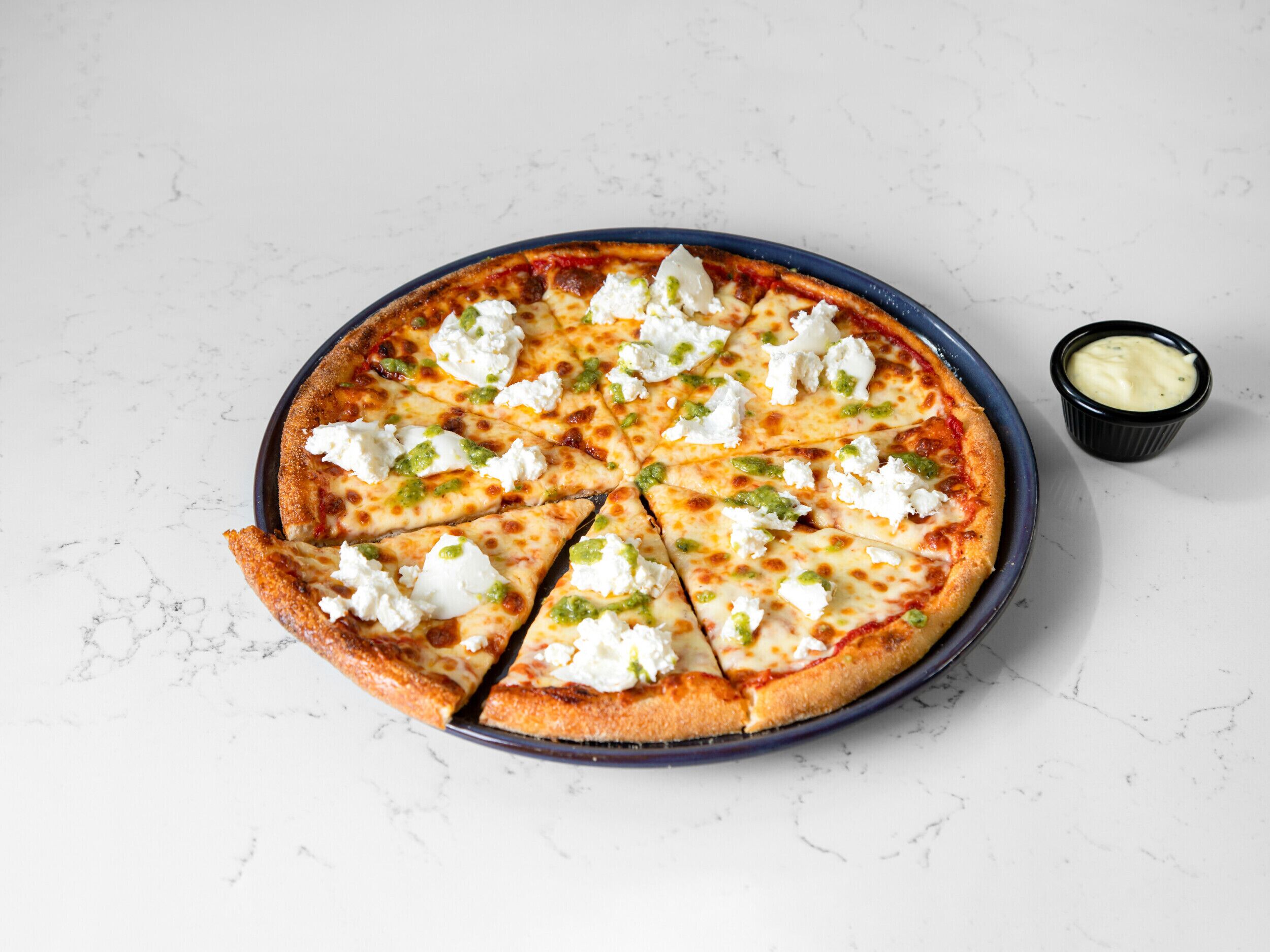 A pizza with cheese and green toppings on a white marble surface.