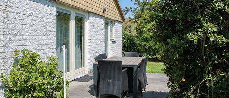 Een gebouw van steen met een houten dak, een terras met rieten meubels en een kleine tuin.