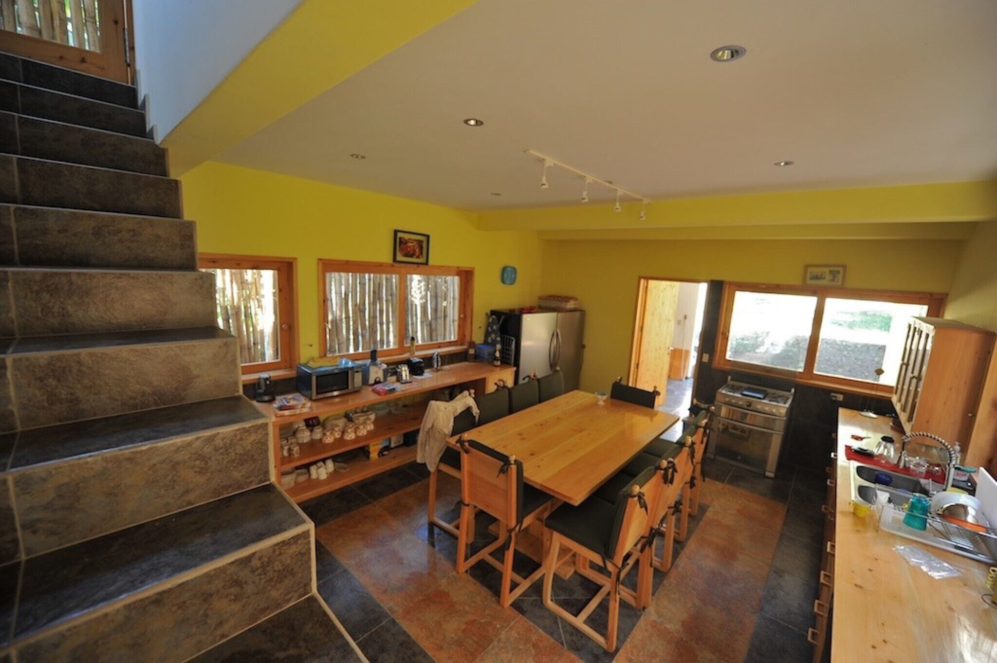 A kitchen with a wooden table, chairs, and a staircase.