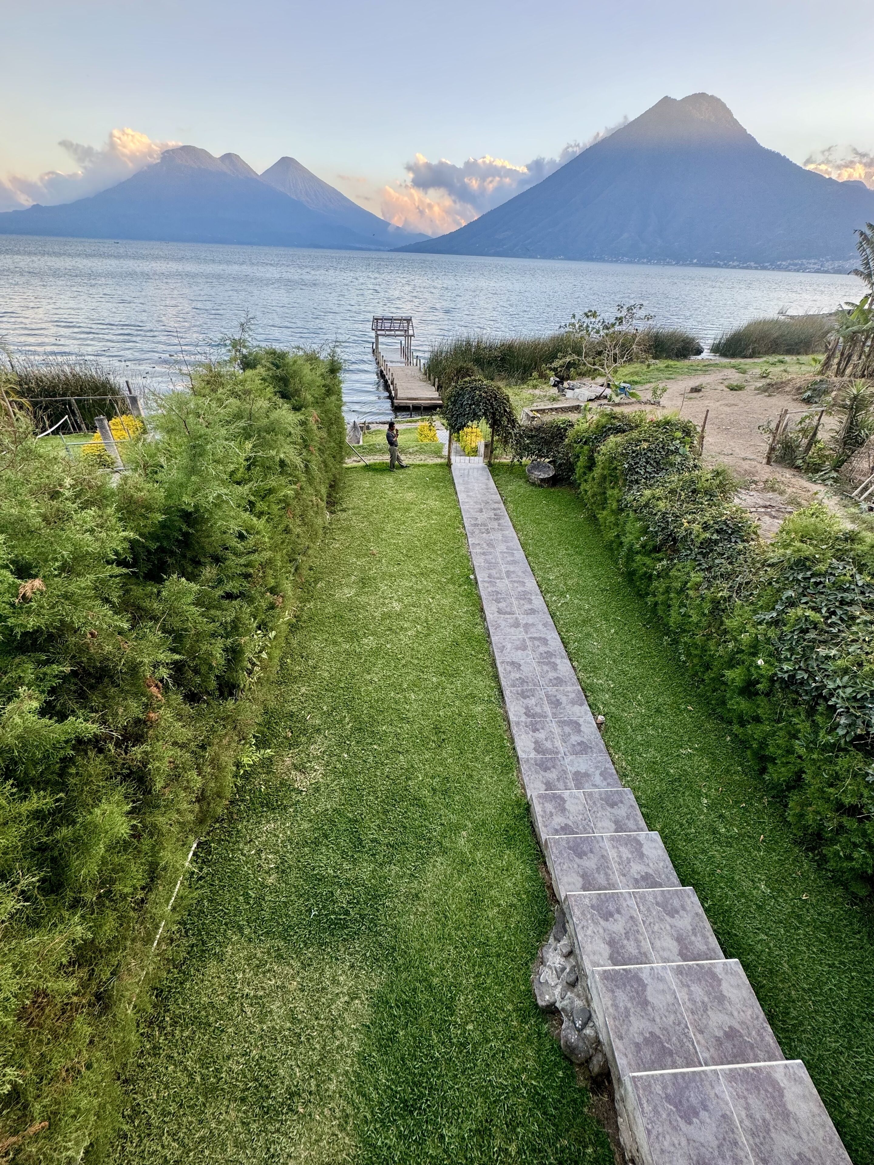 A pathway leading to a dock over a lake with mountains in the background.