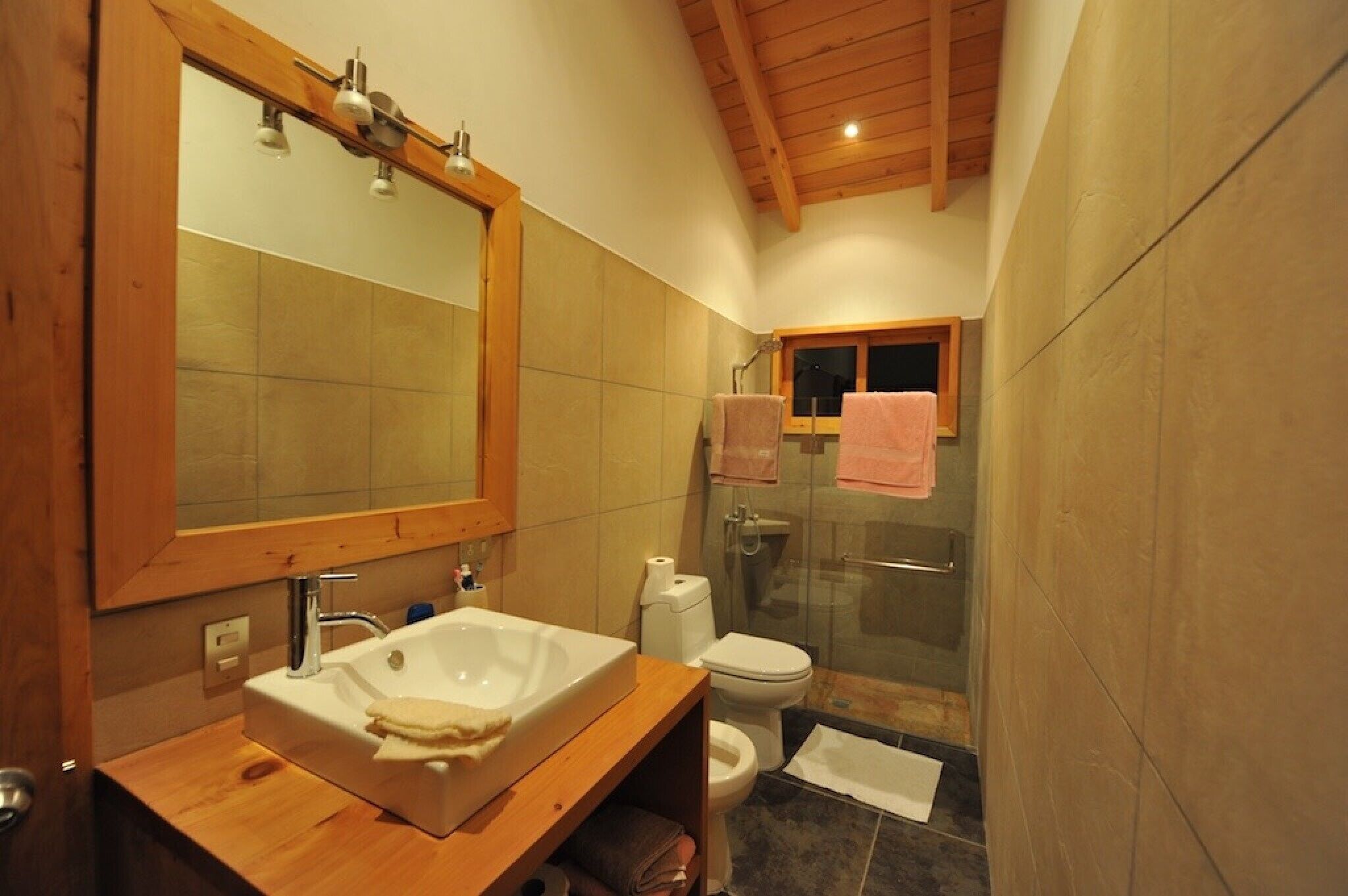 A bathroom with a wooden vanity, a large mirror, a sink, a toilet, and a glass-enclosed shower.