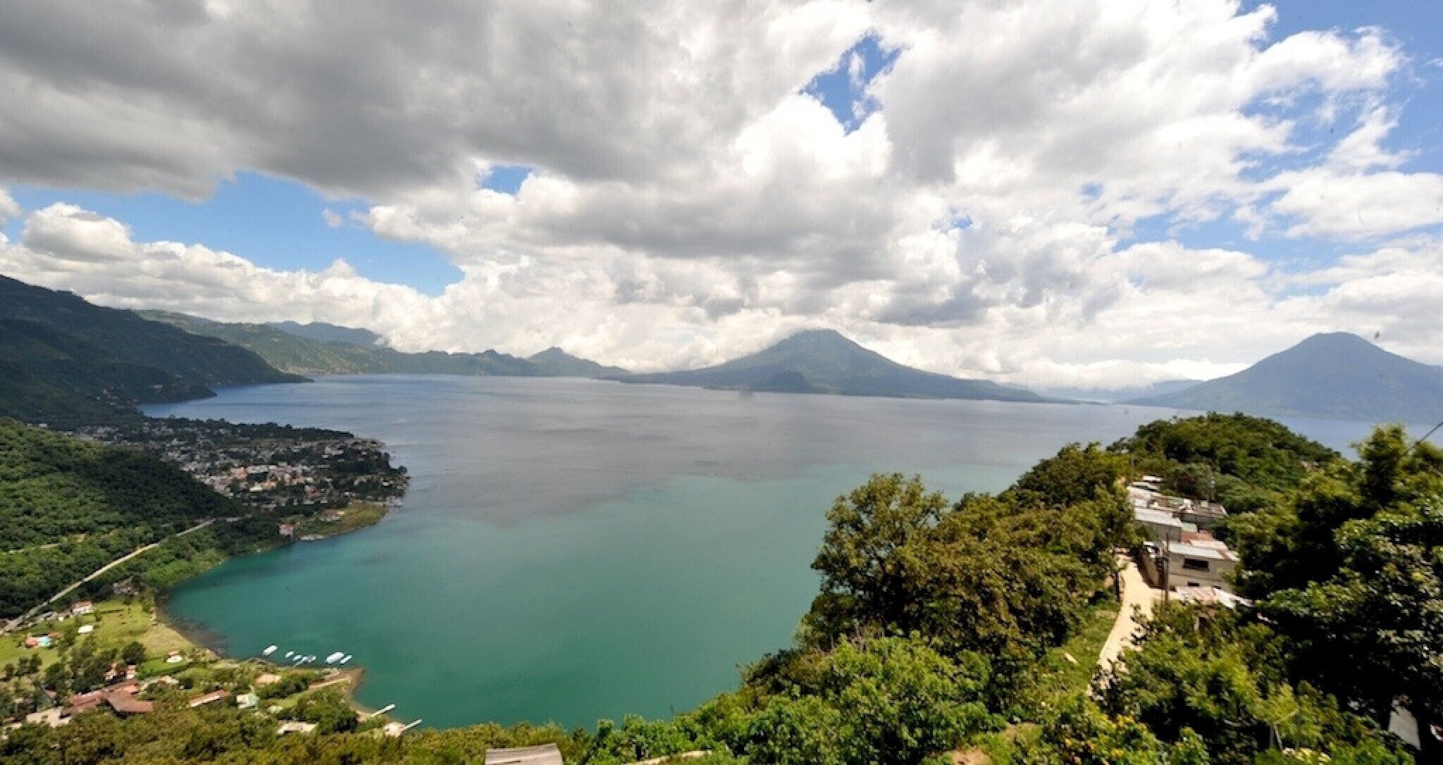 A panoramic view of a coastal town with a large body of water, mountains in the background, and a clear sky.