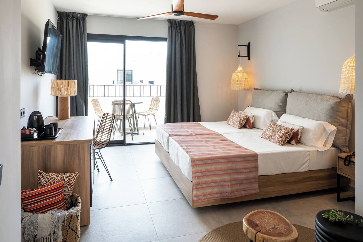 Une chambre d’hôtel moderne équipée d’un lit, d’un bureau, d’une chaise, d’un balcon et d’une télévision.