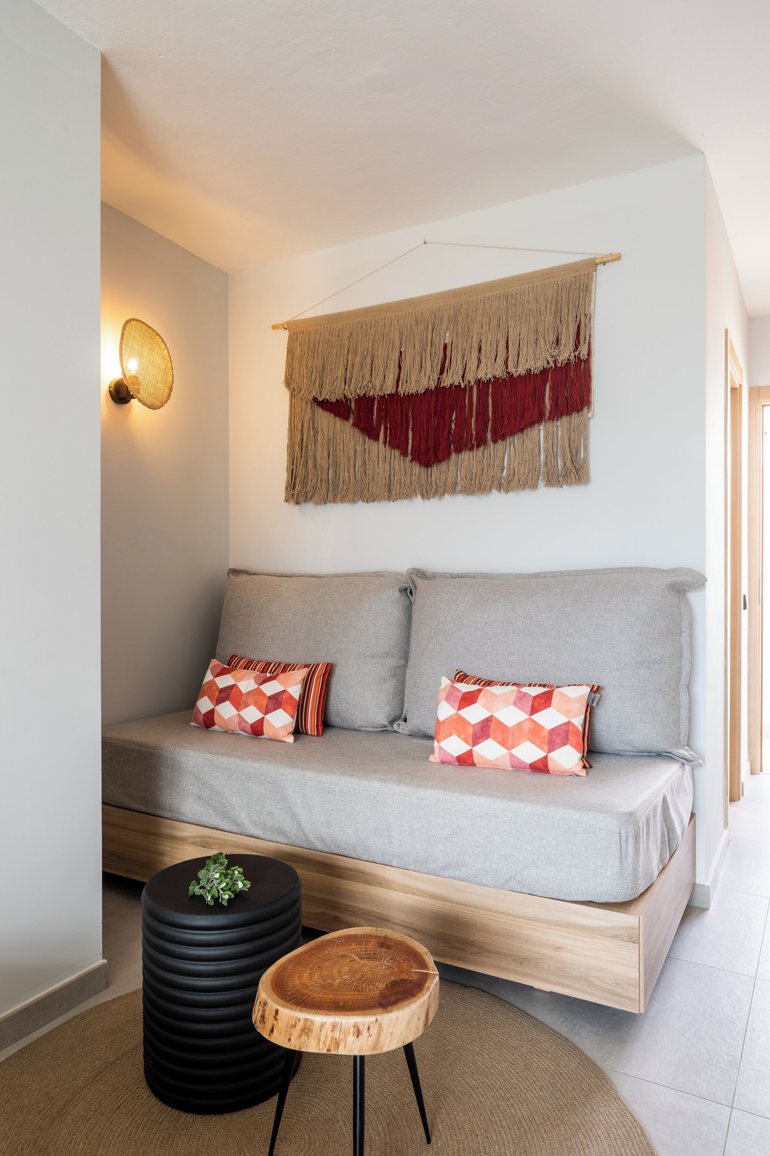 Una sala de estar moderna con un sofá gris, dos cojines estampados, una mesita auxiliar redonda negra y una mesita auxiliar de madera con una planta.