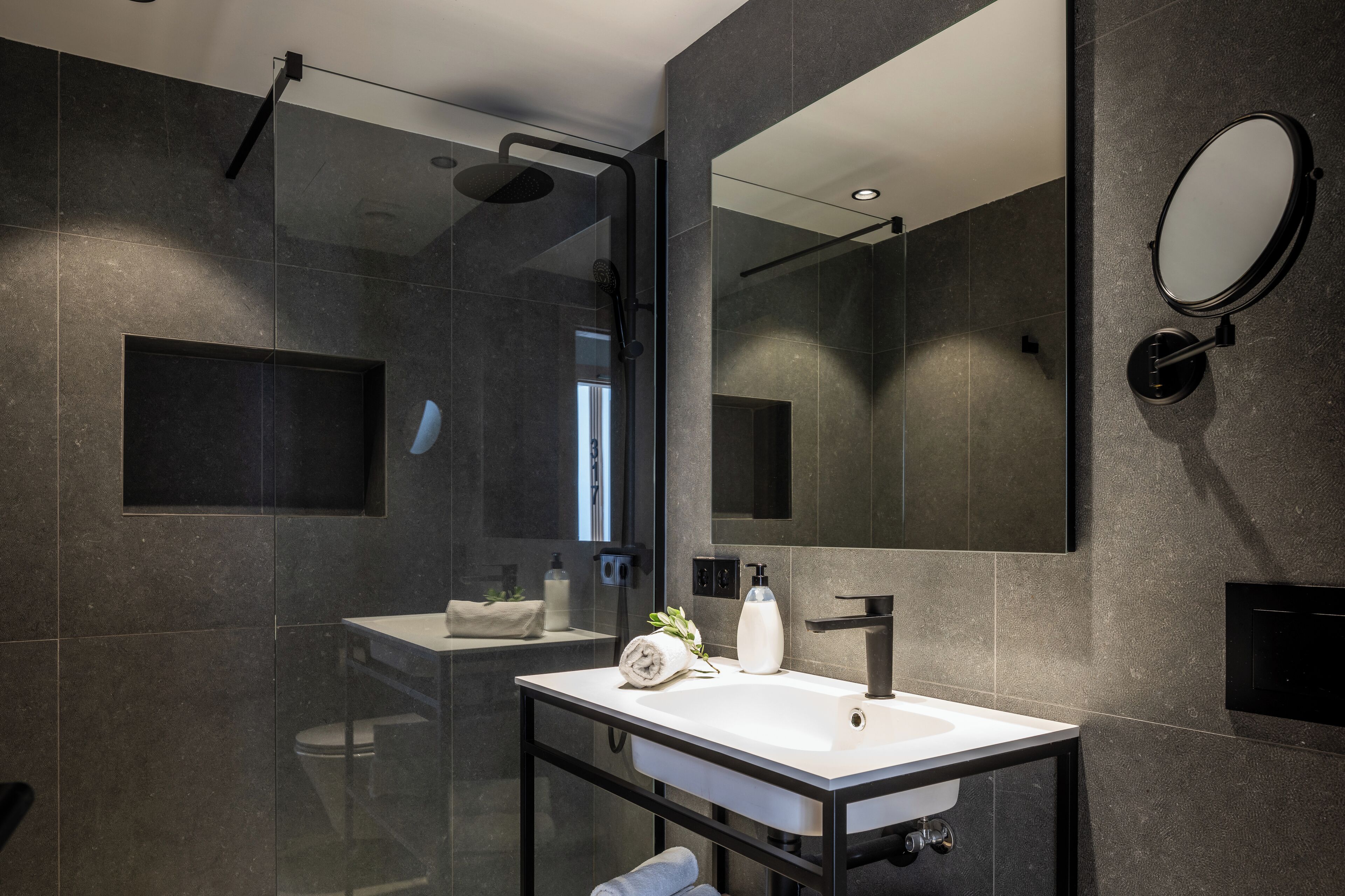 A modern bathroom with a glass-enclosed shower, a large mirror, and a white sink.