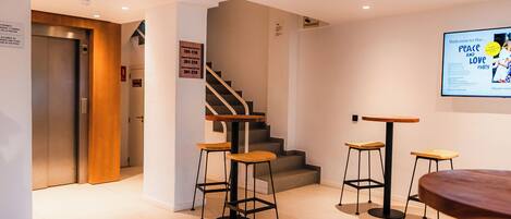 A modern hotel lobby with a staircase, a reception desk, and a bar area with stools.