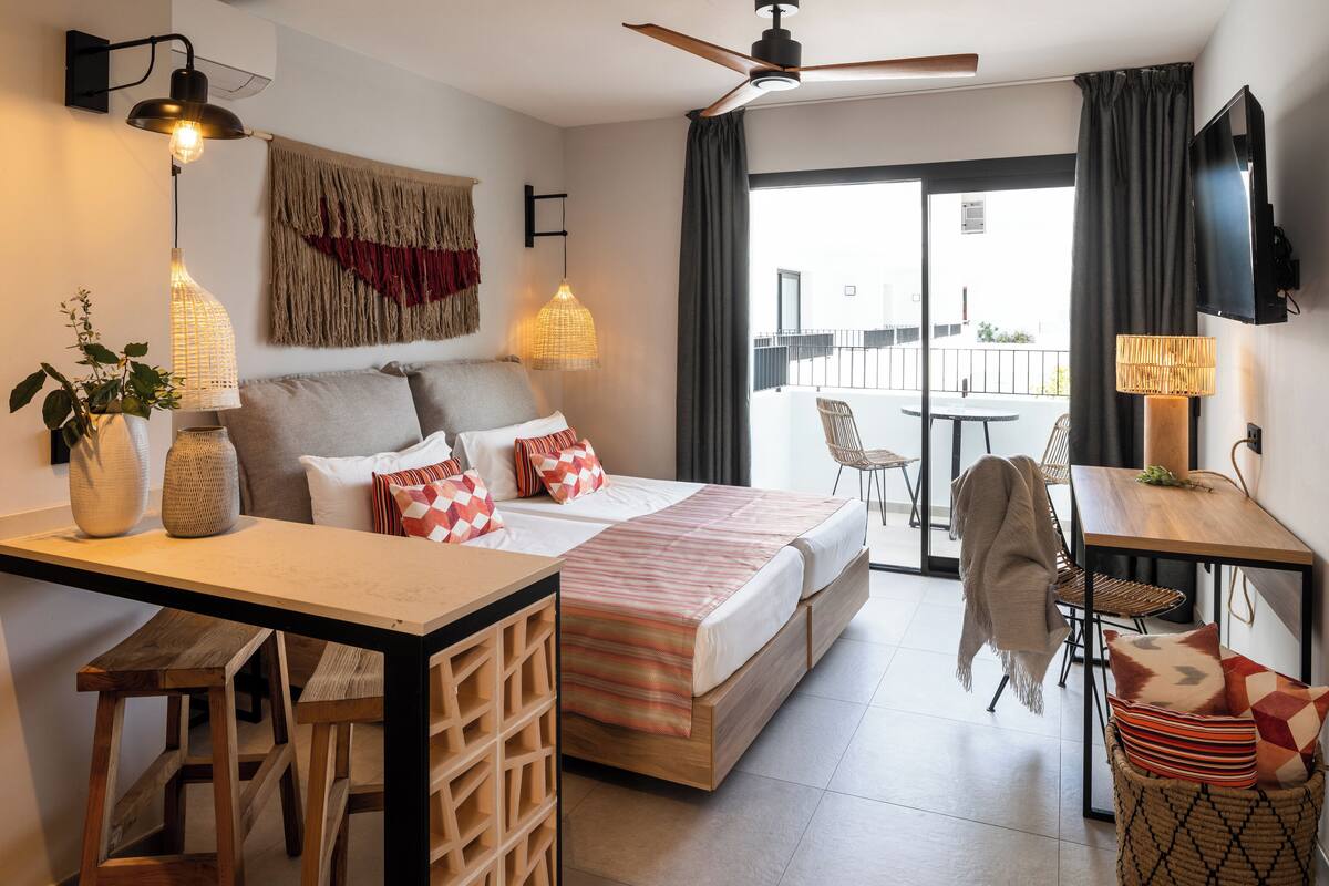 Une chambre d’hôtel moderne équipée d’un lit, d’un bureau, d’une chaise et d’un balcon avec une table et des chaises.