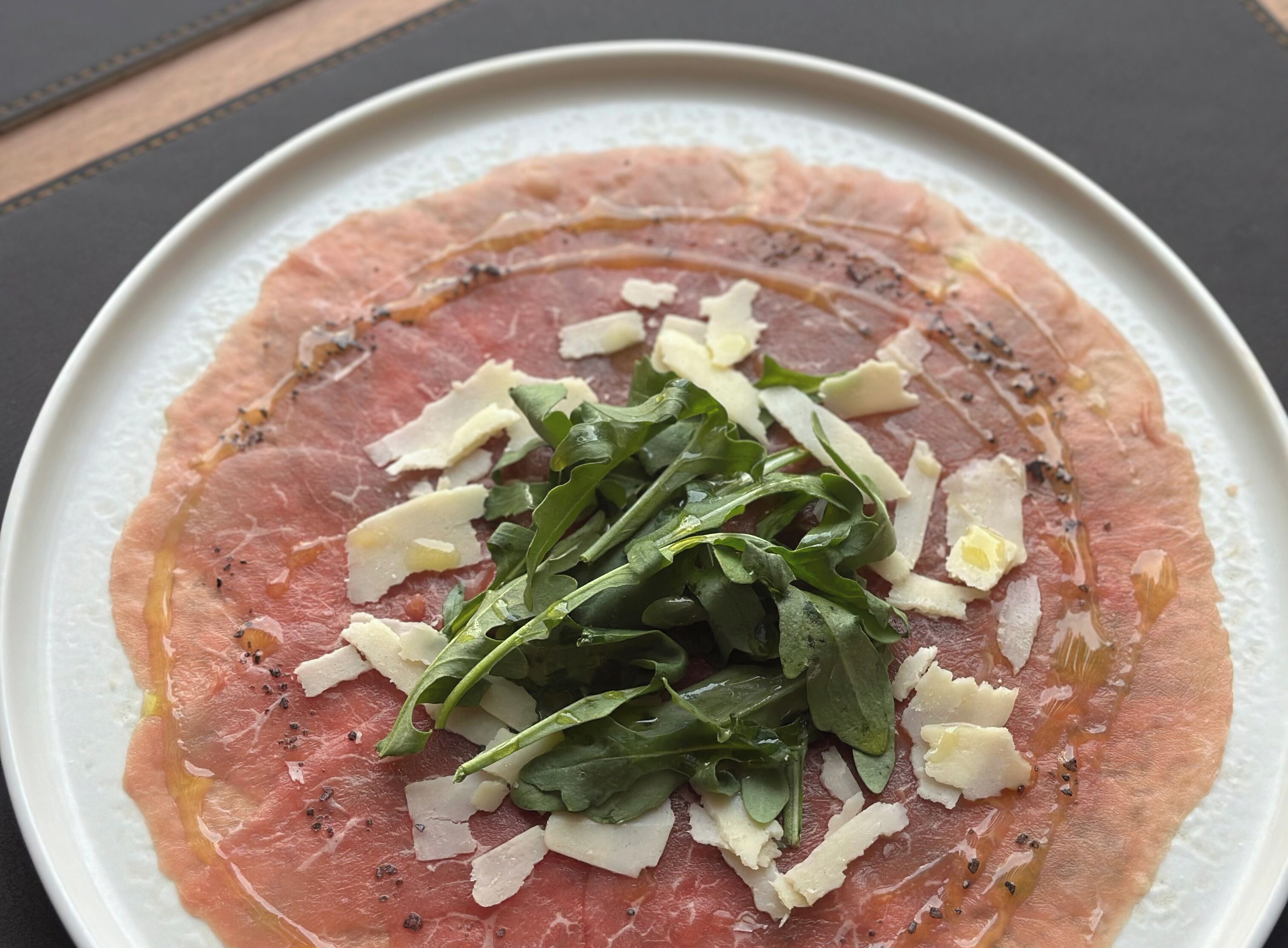 Une assiette de viande crue, accompagnée de fromage et de légumes verts.