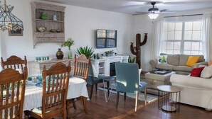A dining area with wooden chairs and a table, a blue chair, a white sofa with colorful cushions, and a cactus sculpture.