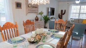 A dining area with a round table set for four, wooden chairs, a vase with flowers, and a television in the background.