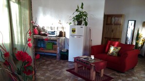 Un salon avec un canapé rouge, une table basse, un réfrigérateur et une plante en pot.