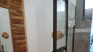 Une salle de bain avec une porte en bois, des toilettes blanches, une cabine de douche en verre et une serviette blanche accrochée à la porte de la douche.