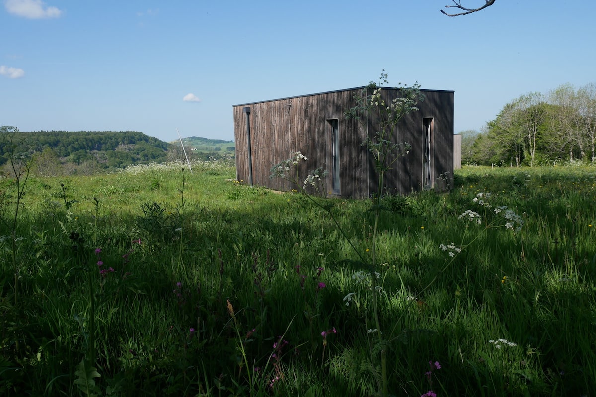 Un bâtiment rustique en bois, situé dans un champ verdoyant sous un ciel dégagé.
