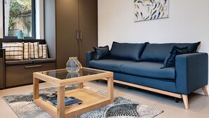Een moderne woonkamer met een blauwe bank, een glazen salontafel en een groot raam.