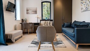 Een moderne woonkamer met een bank, een bureau en een stoel. Er is een raam met uitzicht op bomen, een wereldbol op het bureau en een schilderij aan de muur.
