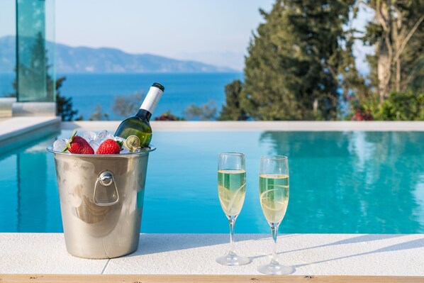 A poolside setting with a bucket containing a bottle of wine and strawberries, and two glasses of wine.