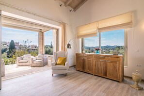 A spacious room with a large window offering a city view, a wooden cabinet, and a comfortable seating area with a chair and sofa.