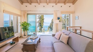 Ein geräumiges Wohnzimmer mit einem großen Fenster, das einen malerischen Blick auf das Meer und die Berge bietet.