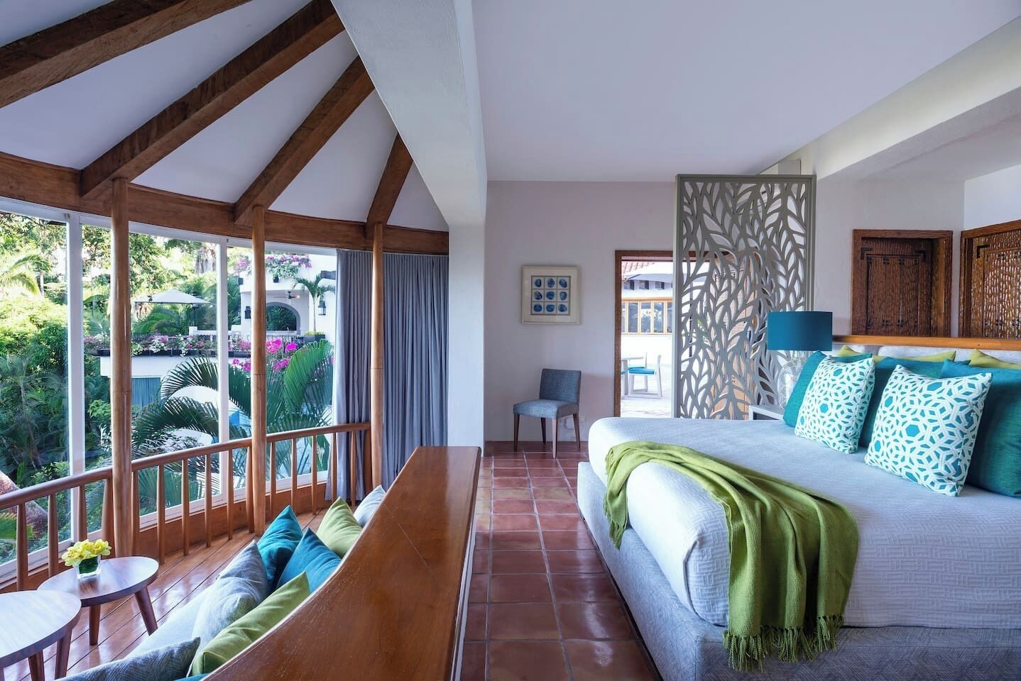 A room with a bed, a seating area with a table, and a view of greenery outside.