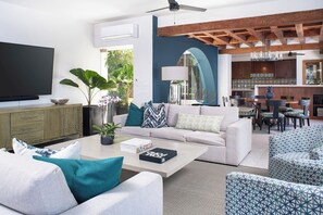 Una sala de estar moderna con sofá, mesa de centro y televisor. Hay una zona de cocina con mesa y sillas.