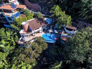 A residential property with a swimming pool, surrounded by lush greenery and a red-tiled roof.