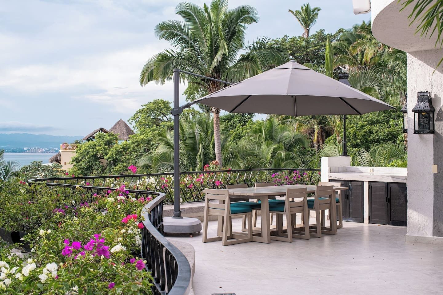 An outdoor patio with a table and chairs, a large umbrella, and a view of the ocean.