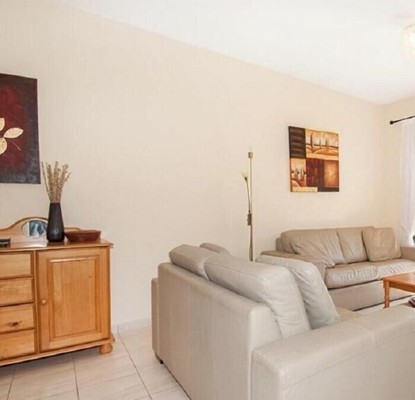Un salon comprenant un canapé, un meuble en bois et deux œuvres d’art accrochées au mur.