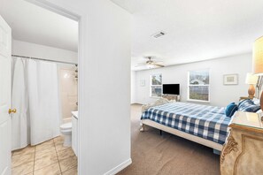 Un dormitorio con cama, ventilador de techo, ventana con persianas y televisión.