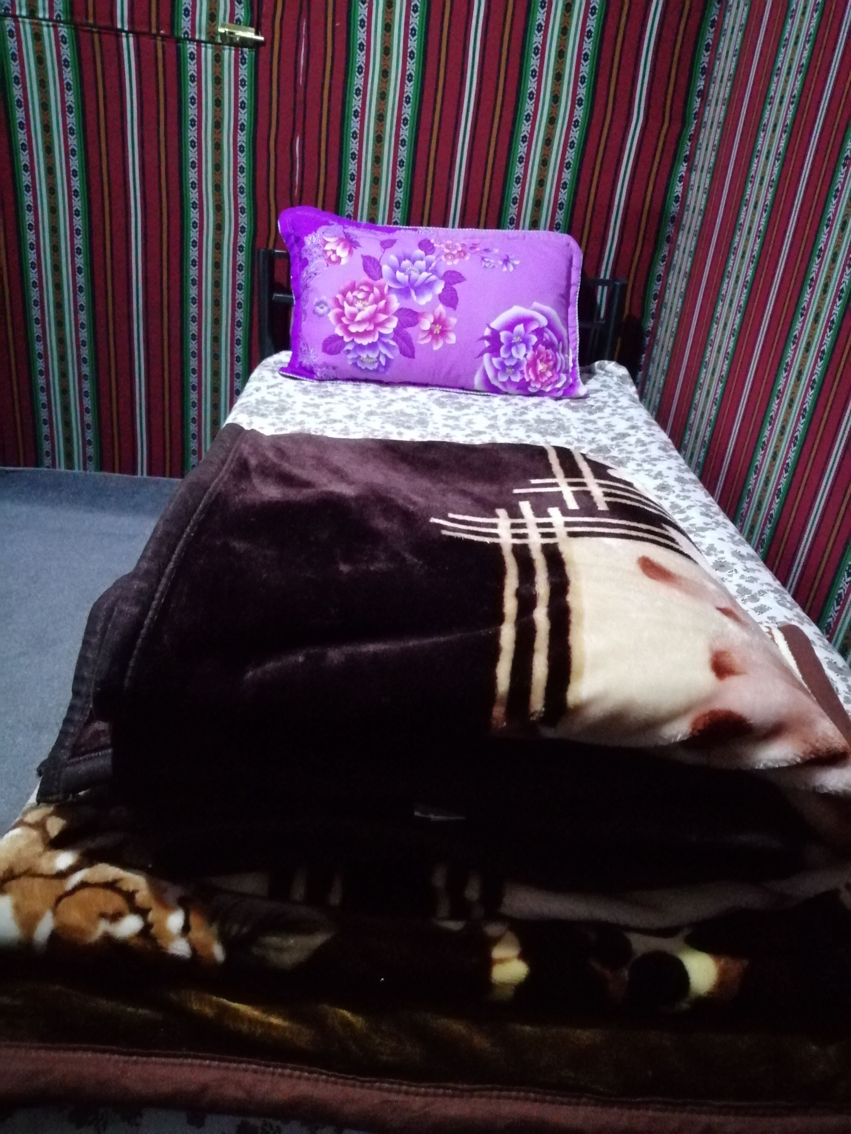 A bed with a purple floral pillow, a dark brown blanket, and a patterned bedspread.