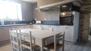 Une cuisine avec une table et des chaises blanches, un four encastré et une fenêtre.
