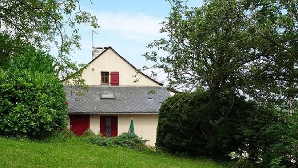 Une maison de plain-pied avec une porte rouge et une petite fenêtre, entourée d’une végétation luxuriante.
