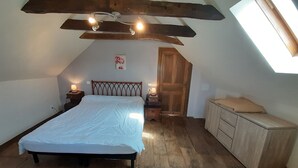 Une chambre avec un plafond en pente, un lit, des tables de chevet, une armoire en bois et un puits de lumière.