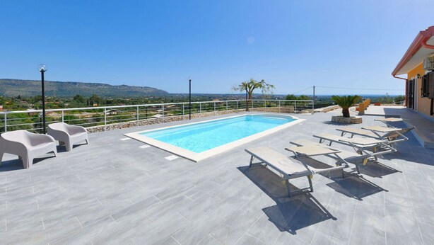 Une piscine sur le toit offrant une vue dégagée sur le paysage, notamment sur les collines et une côte lointaine.