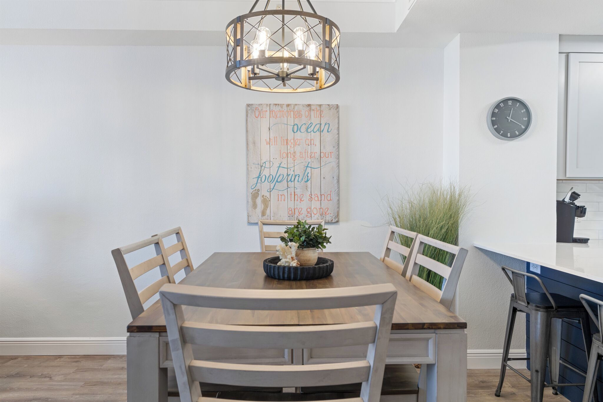 A dining area with a wooden table, four chairs, a chandelier, a clock, and a decorative wall piece.