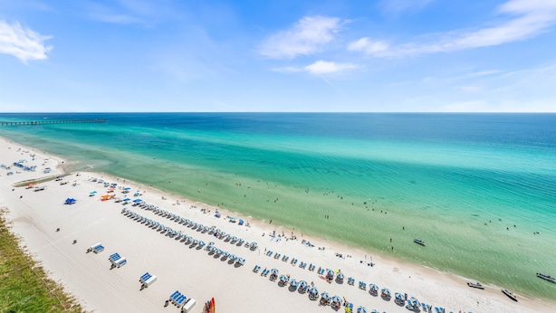 A beach with rows of sun loungers and umbrellas, a pier extending into the ocean, and clear turquoise waters.