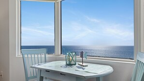 A room with a table and chairs by a window overlooking the sea.