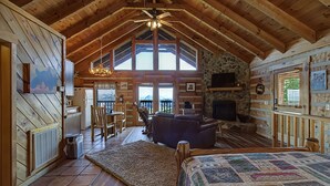 L’intérieur d’une cabane en rondins, avec une chambre à coucher située en mezzanine, une cheminée et un mur en pierre.