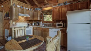Une cuisine rustique aménagée dans une cabane en bois, avec une table à manger, des chaises en bois, un réfrigérateur, un four à micro-ondes et des placards en bois.