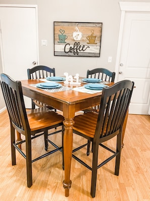 A dining table with six chairs, a coffee-themed wall art, and a white door in the background.