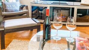 Ett vardagsrum med en soffa, ett soffbord i glas med en flaska rött vin och två vinglas, en platt-TV och en öppen spis.