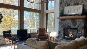 Ein gemütliches Wohnzimmer mit Kamin aus Stein, großen Fenstern, einer bequemen Couch und einem Fernseher.