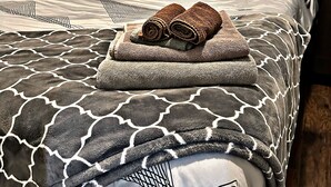 A neatly made bed with patterned bedding, a rolled towel, and a single orange pillow. - Cozy Charming •Art 🎨 • Food🌮 Close to Train 🚉 • Parking! (Chicago)