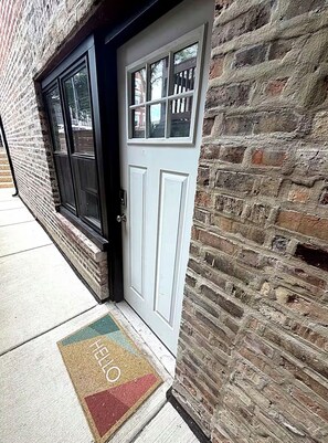 A white door with a window above it, set in a brick wall.