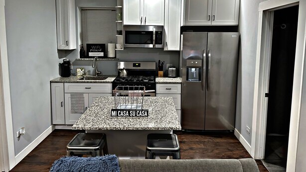 A compact kitchen with white cabinets, a stainless steel refrigerator, a microwave, and a gas stove. - Cozy Charming •Art 🎨 • Food🌮 Close to Train 🚉 • Parking! (Chicago)
