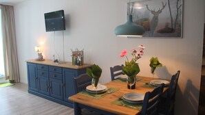 Un comedor con una mesa de madera dispuesta para cuatro, sillas azules y un televisor montado en la pared.