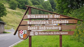 Señal de madera de bienvenida para un parque nacional en Sankt Andreasberg, con el logotipo de la UNESCO y un escudo de armas.