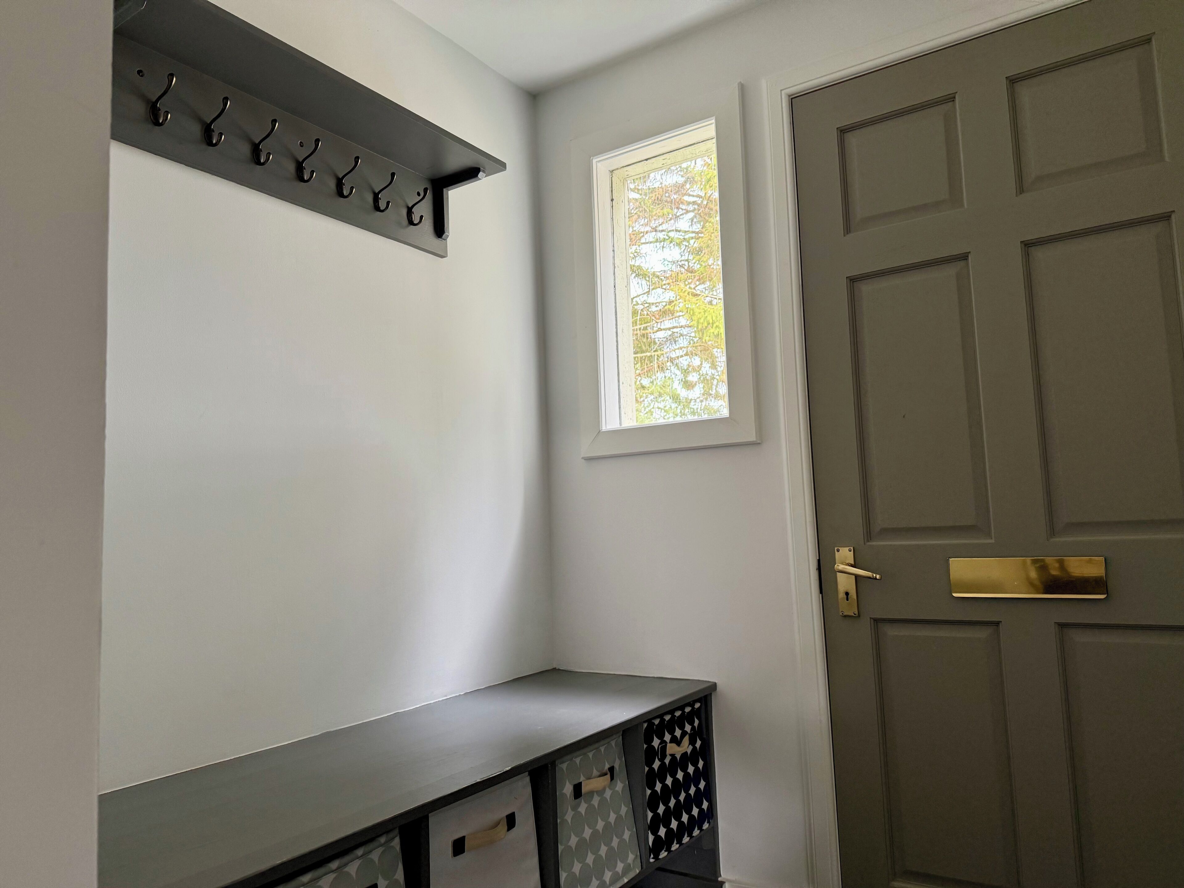 A hallway with a coat rack, a window with a view of trees, and a door with a brass handle.
