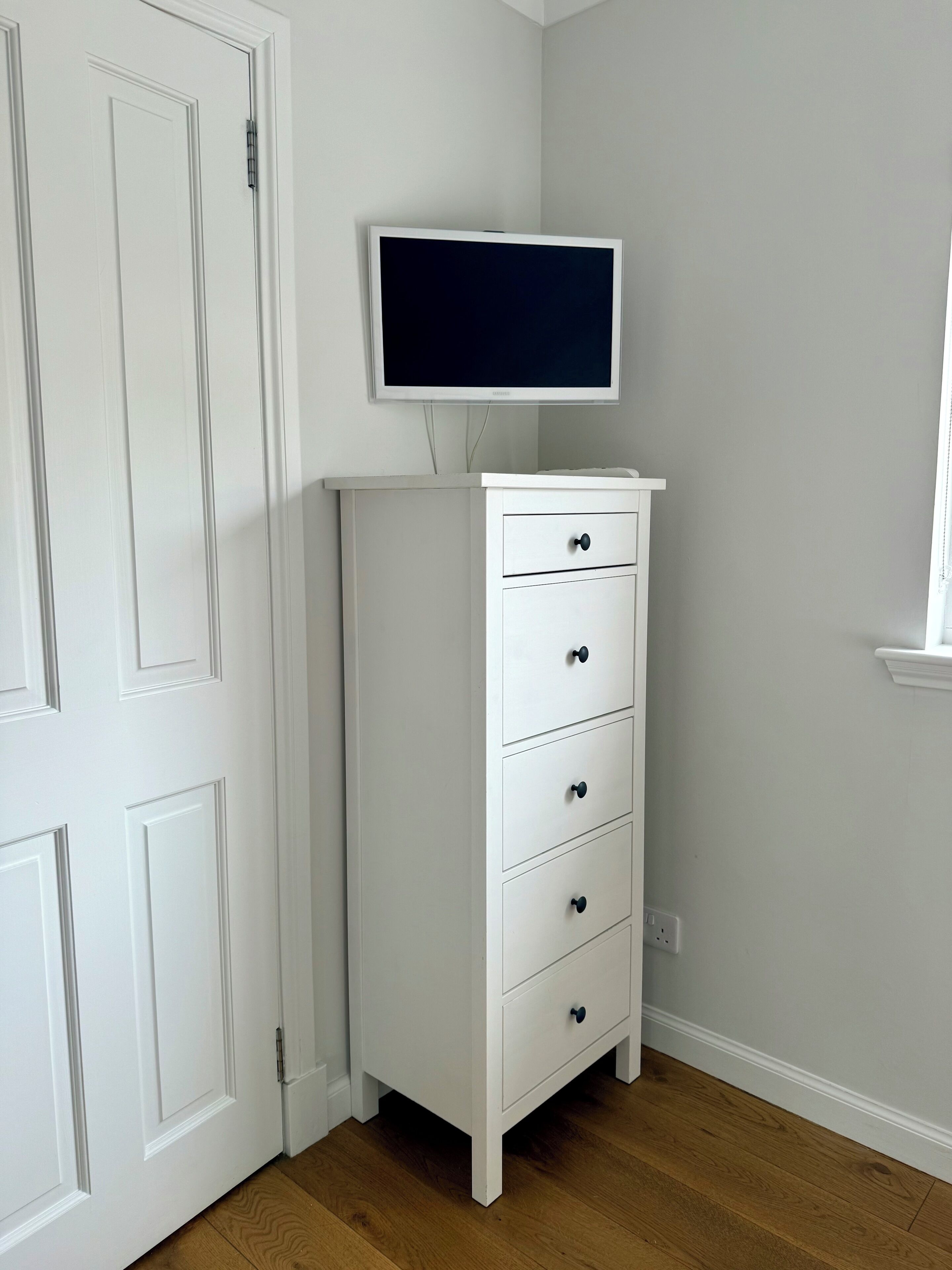 A white dresser with drawers and a flat-screen TV mounted above it.