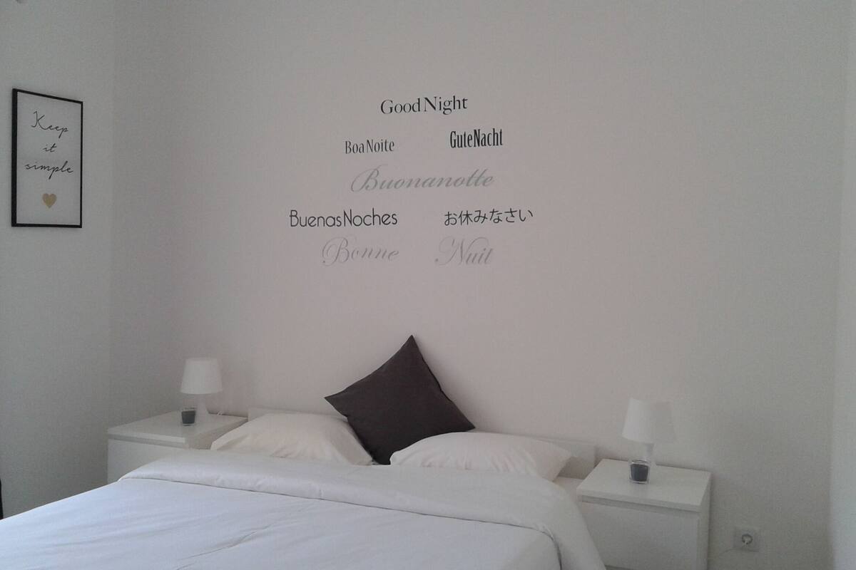 Une chambre à coucher avec un lit, deux tables de chevet et un mur orné de messages « Bonne nuit » dans différentes langues.
